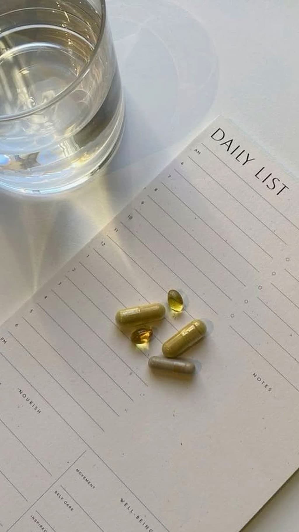 Copo de água, planner e suplementos sobre a mesa, em luz natural